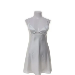 Vit satinliknande klänning från Zara - Supersnygg vit kortklänning från Zara i satinliknande polyester. Klänningen har tunna axelband, öppen rygg med snygga banddetaljer och en lätt utsvängd passform. Perfekt för sommarkvällar eller när du vill känna dig extra chic.