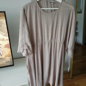 Ljusbeige klänning från Only Trend - Luftig ljusbeige klänning från Only Trend i storlek 38. Modellen har trekvartsärmar med snygg snörningsdetalj, rund halsringning och lätt rynkad midja. Materialet är tunt och strukturerat, perfekt för en chill och avslappnad look.