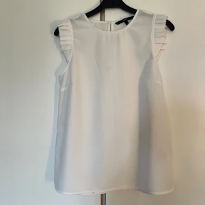Vit ärmlös blus från Vero Moda - Superfin vit blus från Vero Moda i storlek S. Den är ärmlös med snygga plisserade detaljer på axlarna och har en rak, luftig passform. Perfekt till jeans eller kjol när du vill ha en clean och fräsch look.