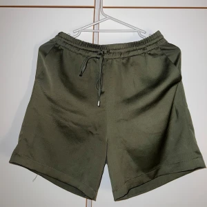 Olivgröna shorts från Vila med snörning - Snygga olivgröna shorts från Vila i storlek 36. De har elastisk midja med snörning för skön passform och är tillverkade i ett mjukt, lätt material. Perfekta för varma dagar och chill outfits.