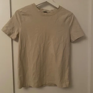Beige t-shirt från Zara - Enkel och stilren beige t-shirt från Zara i storlek S. T-shirten har rund halsringning och korta ärmar, perfekt för en clean och avslappnad look. Tillverkad i mjuk bomull som känns skön mot huden.