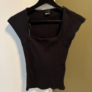 Svart ribbad topp från Gina Tricot - Svart ribbad topp från Gina Tricot med fyrkantig ringning och breda axlar. Toppens material är stretchigt och sitter tight mot kroppen. Perfekt för dig som gillar en enkel men stilren look.
