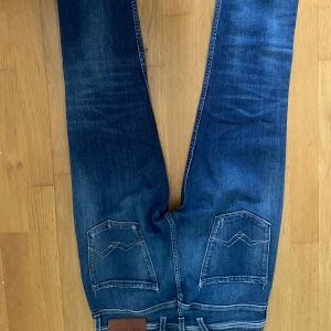Blå Replay jeans med slitningar - Snygga blå jeans från Replay med coola slitningar och klassiska bakfickor med broderad detalj. Jeansen har normal passform och raka ben, tillverkade i mjukt denimtyg som sitter skönt hela dagen.