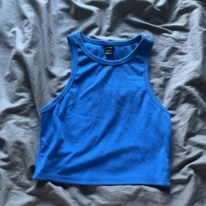 Blå ribbad linnetopp från SHEIN - Snygg blå ribbad linnetopp från SHEIN i storlek S. Toppen är ärmlös med hög halsringning och croppad passform, perfekt för varma dagar eller att styla lager på lager. Enkel och stilren design som är lätt att matcha med jeans eller kjol.