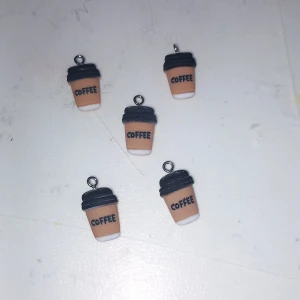 Örhängen med kaffemugg-berlocker - Söta örhängen formade som små takeaway-kaffemuggar med svart lock och texten 'COFFEE' på framsidan. Muggarna är beige med vit botten och har en trendig och lekfull design, perfekta för kaffeälskare.