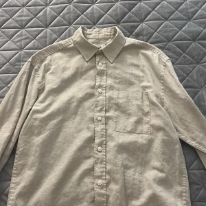 Beige linneskjorta från H&M, relaxed fit - Snygg beige skjorta från H&M i relaxed fit. Skjortan är tillverkad i linne, har klassisk krage, bröstficka och knäppning framtill. Perfekt för en chill och stilren look. Långärmad och passar dig som gillar en luftig och enkel stil.