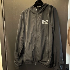 Windbreaker från Armani  - Stilig svart windbreaker från Armani. Fräsch design och väldigt skön att ha på sig. Den är storlek M. Knappt använd så mycket bra skick. Hör av er om eventuella frågor och funderingar.