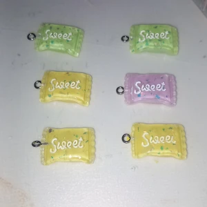Färgglada godisberlocker "Sweet" - Säljer söta berlocker formade som godispåsar med texten "Sweet". Finns i pastellgul, ljusgrön och ljuslila med små färgglada detaljer. Perfekta att använda till halsband, armband eller örhängen för en lekfull look.
