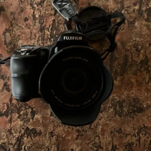 Fujifilm proffsiga finepix kamera  - en Fujifilm-kamera med superzoom i toppskick! optisk zoom (28-300 mm), bildstabilisering. ansiktsdetektering, skarpa bilder i svagt ljus, RAW-stöd. Perfekt för proffsiga bilder för resor, natur eller vardagsfotografering. Testad & redo – fånga detaljer på avstånd! Kort, laddare och allt ingår 