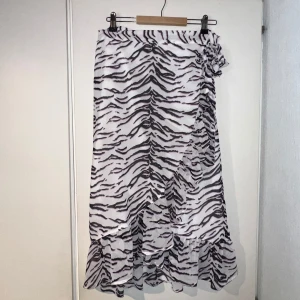 Zebramönstrad omlottkjol från BikBok - Säljer en superfin omlottkjol från BikBok i zebramönster med svart, vitt och en hint av rosa. Kjolen har volangkant nertill och knyt i sidan för extra detalj. Nyskick! Passar allt från S-XL. Justera själv ❤️
