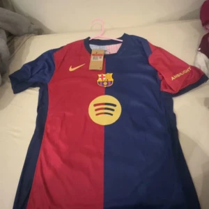 FC Barcelona matchtröja Nike L - Säljer en officiell FC Barcelona matchtröja från Nike i storlek L. Tröjan har klassisk halva-röd halva-blå design, klubbmärke och Nike-logga på bröstet samt Spotify och Ambilight-tryck. Tillverkad i lätt och ventilerande material, perfekt för fotbollsälskare.