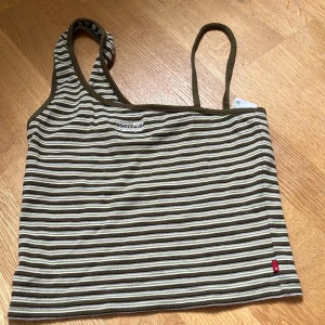 Randig linnetopp från Levi's - Snygg randig linnetopp från Levi's i olivgrönt och vitt. Topp med tunna axelband och broderad logga framtill. Perfekt för varma dagar och enkel att matcha med jeans eller shorts. Har använts cirka 2 gånger då den var i fel storlek. Klicka EJ på köp nu och om du har fler frågor : skriv!❤️ (den passar S/M/L)