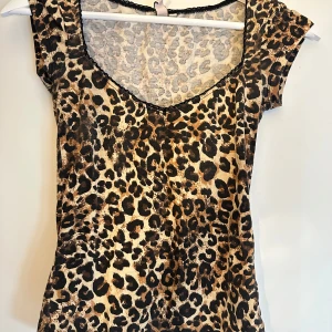 Leopardmönstrad topp från Nelly XXS - Snygg leopardmönstrad topp från Nelly i figurnära modell. Toppen har korta ärmar, djup rundringning med svart spetskant och är gjord i mjukt stretchigt material. Passar även Xs
