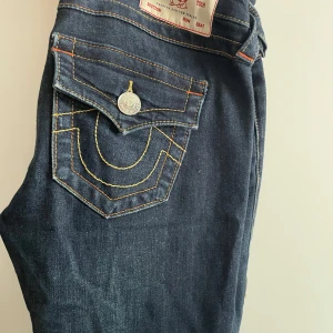 Mörkblå low waist bootcut true religion jeans - Säljer ett par mörkblå low waist bootcut jeans från True Religion med snygga detaljer på fickorna. Jeansen är i storlek 24 men är uppsydda så det passar någon som är ca 160-166 cm. De är använda ett fåtal gånger så det är i mycket bra skick. Nypris 1300kr. Skriv om ni har frågor eller är intresserade!
