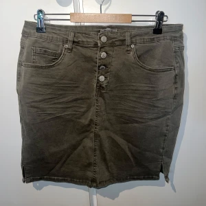 Olivgrön jeanskjol med knappar - Olivgrön kort jeanskjol från Sincerely Lou med fyra synliga knappar framtill, klassiska jeansfickor och bälteshällor. Kjolen har en rak passform och små slitsar i sidorna för extra rörelsefrihet. Perfekt att styla med sneakers eller boots. Använd fåtal gånger. Passar M-L ❤️