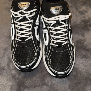 Dior B30 svarta sneakers strl 44 - Snygga Dior B30 sneakers i svart med vita och silverfärgade detaljer. Skorna har mesh och syntetmaterial, tydlig Dior-logga på sidan och CD-detalj bak. Tjock vit sula och vita snören ger en sportig och exklusiv vibe. Perfekta för dig som vill sticka ut. Priset kan absolut diskuteras vid snabbt affär;)