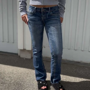Lågmidjade bootcut jeans - Blå lågmidjade jeans med design på fickorna. Innerbenslängd: 82cm, midja: 40cm💙 personen på bilden är ca 164cm