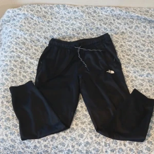 Svarta mjukisbyxor The North Face M - Svarta mjukisbyxor från The North Face i storlek M. Byxorna har dragsko i midjan, dragkedjeförsedda fickor och meshfoder. Logga på benet och tryckt text bak. Perfekta för chill eller träning.