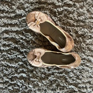 Glittriga ballerinaskor med rosett - Snygga ballerinaskor från Cocorose London i glittrig beige ton med små paljetter och en stor rosett framtill. Skorna har rund tå och platt sula, perfekt för dig som vill ha något både gulligt och trendigt. Materialet är syntet med skinnliknande innersula.