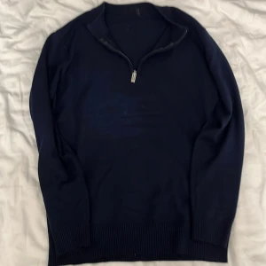 Mörkblå cashmere half zip-tröja - Mörkblå cashmere tröja med half zip-dragkedja i halsen. Tröjan har ribbade muddar vid ärmslut och nederkant, samt långärmad modell. Perfekt för lager-på-lager och chill stil.
