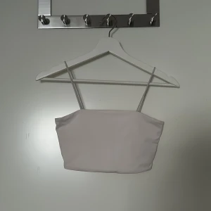 Vit bandeau tubtopp med smala band - Säljer en stilren vit bandeau tubtopp med smala axelband. Toppen har en enkel och clean design som är lätt att matcha med olika outfits. Perfekt för varma dagar eller lager-på-lager-stil.