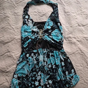 Blommig halterneck topp - Supersöt halterneck topp med blommigt mönster i blått och svart med ett fint glittrigt spänne framtill :)  Supperfin som festtopp!         köpt secondhand, säljer för att den är lite för stor för mig! Står inte storlek men jag uppskattar ca Medium💕