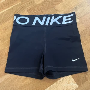 Nike Pro Dri-FIT svarta träningstights-shorts - Svarta Nike Pro Dri-FIT shorts med bred resår i midjan och stor logga. Tight passform och tillverkade i ett stretchigt syntetmaterial som andas. Perfekta för träning och sport. Klassisk Nike Swoosh på benet och diskreta sömmar för en clean look. Aldrig använda. 