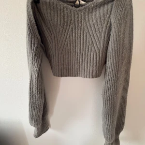 Grå croppad stickad tröja WADAR - Grå croppad stickad tröja med ribbat mönster och lång ärm. Plaggen är väl använda så finns täcken på användning, vilket ni kan se på bilderna. Annonsen finns på flera ställen så skriv till mig innan ni trycker på köp🫶🏻