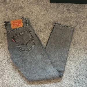 Levi's 502 grå jeans W29 L32 - Säljer ett par Levi's 502 Hi-Ball jeans i snyggt grått tvättat denim. Klassisk femficksmodell med rakt snitt och normal midja. Ikonisk röd Levi's-tag på bakfickan och läderpatch i midjan. Perfekta för en chill och stilren look.
