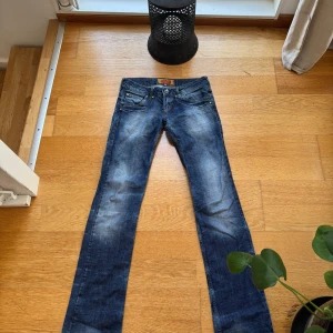 Dsquared2 lågmidjade jeans med detaljer - Snygga blå lågmidjade från Dsquared2 med slitningar och coola detaljer som dekorativa nitar och unik patch med metallmärke bak.
