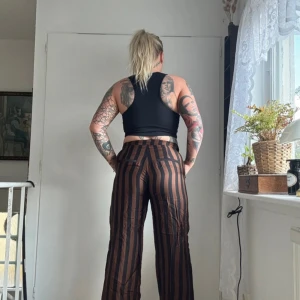 Brun- och svart-randiga wide byxor - Säljer ett par bruna och svarta byxor med vertikala ränder och breda ben. Byxorna har hög midja och avslappnad passform, perfekta för en chill och trendig look. Materialet känns lätt och luftigt, och de har fickor på sidorna.