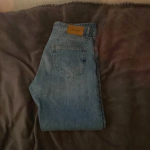 Blå jeans från Jack & Jones - Klassiska blå jeans från Jack & Jones med raka ben och snygg vintagekänsla. Jeansen har en enkel bakficka och detaljer i brunt läder vid linningen. Perfekta för dig som gillar en tidlös och avslappnad stil.