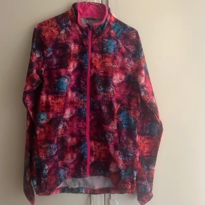 Färgstark vindjacka från SOC, stl 40 - Säljer en riktigt cool vindjacka från SOC i storlek 40. Jackan har ett färgstarkt abstrakt mönster i rosa, blått och rött, hel dragkedja framtill och en praktisk ficka med dragkedja på ryggen. Perfekt för dig som vill sticka ut när du är ute och rör på dig.