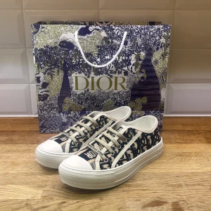 Dior skor - Snygga Dior sneakers med marinblått och beige monogrammönster, vita gummisulor och klassisk snörning. Skorna har tydlig Dior-logga på både plös och sidor, samt stjärndetalj under sulan. Tillverkade i canvas med exklusiv känsla.