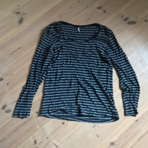 Randig långärmad tröja i bomull - Snygg långärmad tröja med svarta och gråa ränder. Tröjan har en rund halsringning och är gjord i mjuk bomull, perfekt för lager på lager. Passar dig som gillar en enkel men stilren look.