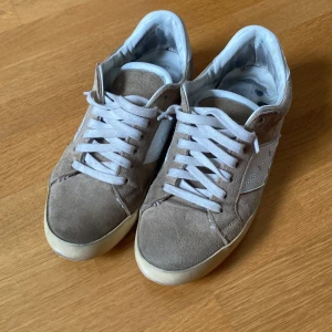 Beige sneakers från Zadig & Voltaire - Snygga beige sneakers från Zadig & Voltaire i mocka och skinn. Skorna har vita detaljer, snörning och en klassisk låg profil. Perfekta för dig som gillar stilrena och trendiga sneakers med en lyxig känsla. Storlek 41 men passar till storlek 40. Nypris på dem här skorna är 2600