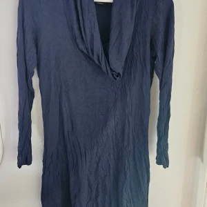 Mörkblå långärmad klänning Lindex - En stilren mörkblå klänning från Lindex i storlek S. Klänningen har lång ärm och en snygg draperad krage som ger en cool touch. Modellen är rak och enkel, perfekt för dig som gillar minimalistisk stil. Materialet känns mjukt och lätt mot huden. Några små tvätt noppror finns 
