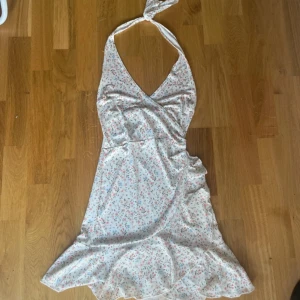 Vit blommig halterneckklänning - Söt kortklänning i vit med små blommor i rosa och blått. Klänningen har halterneck med knyt i nacken, v-ringning och volangkant nertill. Perfekt för varma dagar och somriga vibes. Strl xs. Går att pruta. 