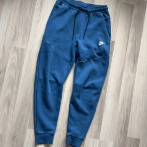 Nike tech fleece byxor  - Snygga blå mjukisbyxor från Nike med svart snörning i midjan och vit logga på låret. Byxorna har ribbade muddar vid bensluten och praktiska fickor. Perfekta för chill eller träning, riktigt sköna och stilrena.