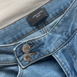 Blå bootcut jeans från Vero Moda XS - Snygga ljusblå jeans från Vero Moda i bootcut-modell. Klassisk femficksdesign, dubbla silverknappar och kontrastsömmar. Jeansen är tillverkade i bomull och har en skön passform med utsvängda ben. Perfekta för dig som gillar en retroinspirerad look. Använda typ 20 gånger men de syns inte.