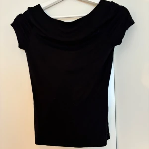 Svart topp med öppen rygg - Säljer en svart croppad topp med korta ärmar och en djup, öppen rygg. Toppen har en enkel och stilren design i mjukt material, perfekt för att skapa en cool och trendig look. Passar grymt till både jeans och kjol. Från Gina Tricot Soft Touch.