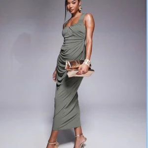 Olivgrön långklänning med drapering - Supersnygg olivgrön långklänning med breda axelband och draperad effekt längs sidorna. Klänningen har en smickrande passform och fyrkantig ringning. Perfekt för dig som vill sticka ut med en stilren och trendig look.