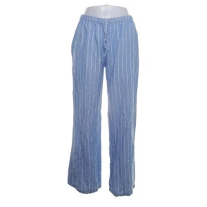 Blå randiga linnebyxor från STR Teen - Blå linnebyxor från STR Teen med vita vertikala ränder och avslappnad passform. Byxorna har resår i midjan med snörning och raka, vida ben. Perfekta för en chill och luftig stil under varma dagar.