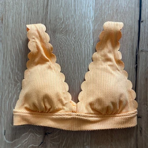 Orange bikiniöverdel med superfina detaljer - Superfin orange bikiniöverdel med vågig kant  och struktur i tyget. Bikinin har justerbara axelband och knytning i ryggen för perfekt passform. 