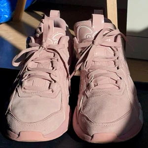 Puma x Hello Kitty rosa sneakers - Chunky sneakers från Puma i samarbete med Hello Kitty. Skorna är ljusrosa med mocka och syntetdetaljer, snörning och vit Hello Kitty-logga tryckt på sulan. Ikonisk Hello Kitty-rosett på sidan och Puma-logga bak. Perfekta för dig som vill sticka ut med en söt och unik stil.
