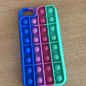Färgglad pop it mobilskal - Säljer ett pop it mobilskal i silikon med coola färger i blått, lila, rosa, rött och grönt. Skalet har bubblor som går att trycka på för extra fidget-faktor och passar perfekt för dig som gillar att pilla. Unik design som sticker ut i mängden!