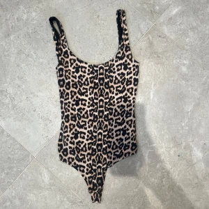 Leopardmönstrad ärmlös bodysuit - Snygg ärmlös bodysuit med leopardmönster i beige och svart. Djup rundad ringning och smala axelband ger en cool och trendig look. Perfekt att styla med jeans eller kjol för en edgy vibe.