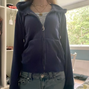 Blå velour hoodie från Juicy Couture - Säljer en blå velour hoodie från Juicy Couture med dragkedja och huva. Jackan har broderad JC-logga på bröstet, snörning i huvan och känguruficka framtill. Perfekt för en chill och trendig look.