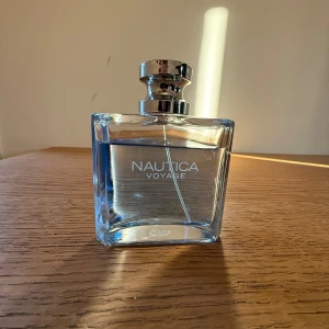Nautica Voyage parfym 100ml - Fräsch parfym från Nautica, Voyage, i en stilren transparent glasflaska med silvrig metallkork. Flaskan är fyrkantig med rundade kanter och rymmer 100ml. Doften är känd för sina marina och fruktiga toner, perfekt för dig som gillar en fräsch och sportig vibe. Lite av parfymen är använd 