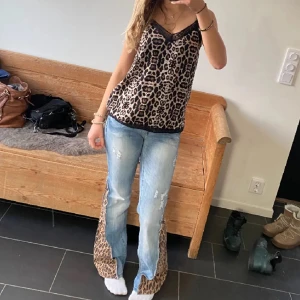 Leopardmönstrad linnetopp med spets - Snygg linnetopp med leopardmönster i beige och svart. Toppen har tunna axelband, v-ringning och svart spetskant upptill. Perfekt för dig som vill sticka ut med ett djurmönstrat plagg och gillar trendiga detaljer.